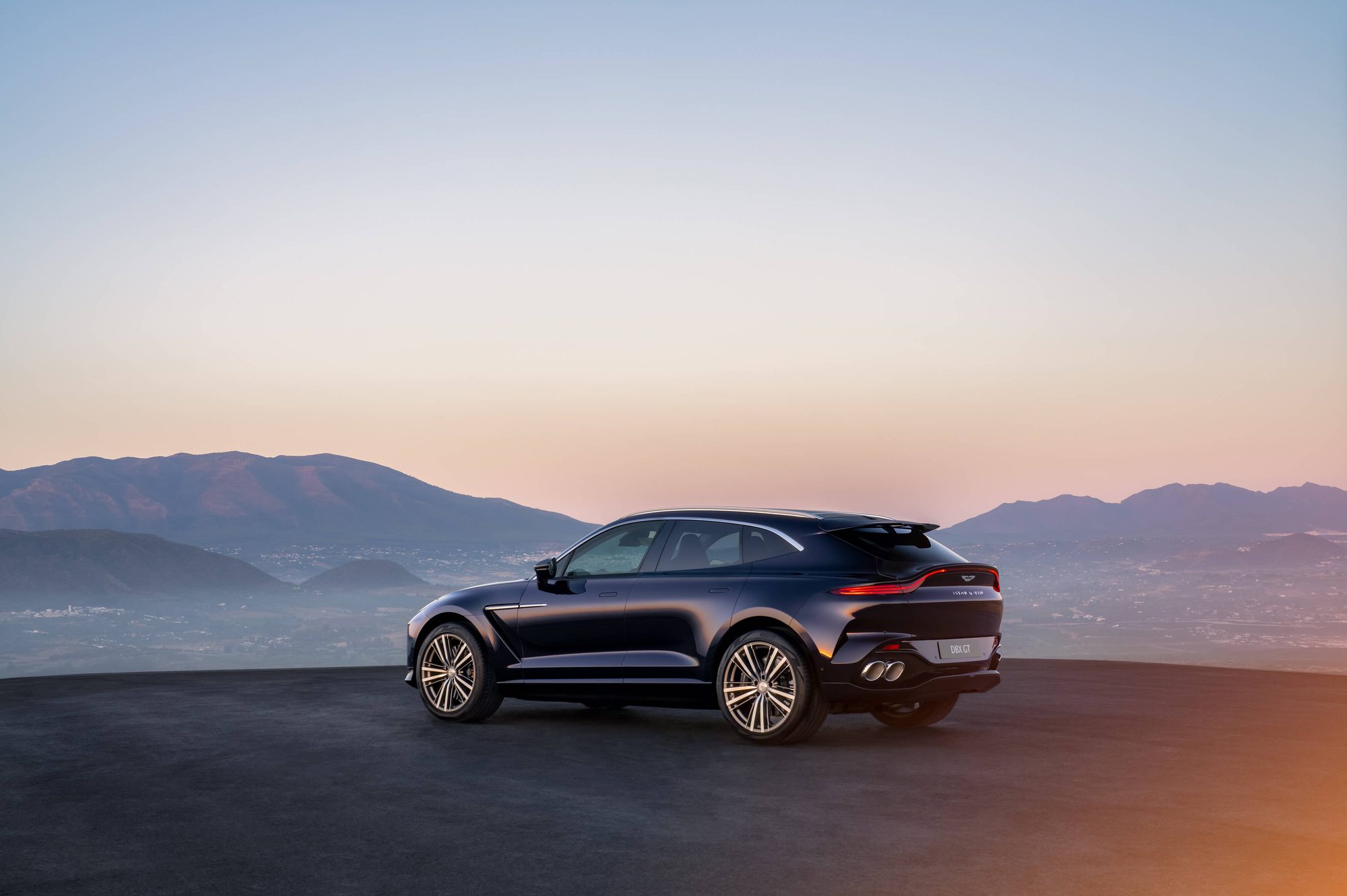 Aston Martin DBX GT en tres cuartos trasero con montañas al fondo