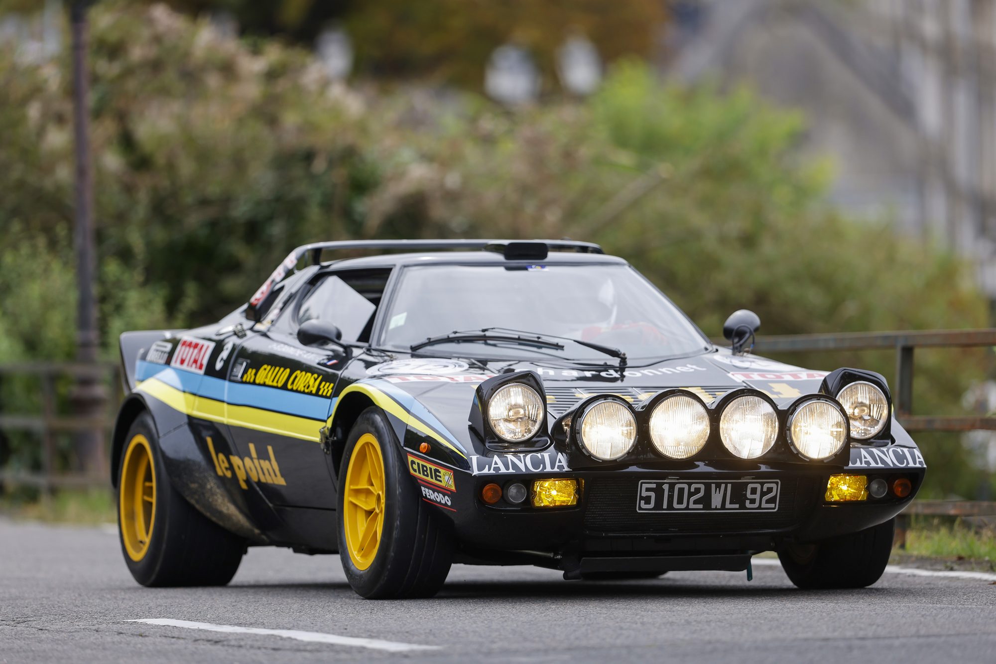 Lancia Stratos negro y amarillo con faros auxiliares en un evento de rally